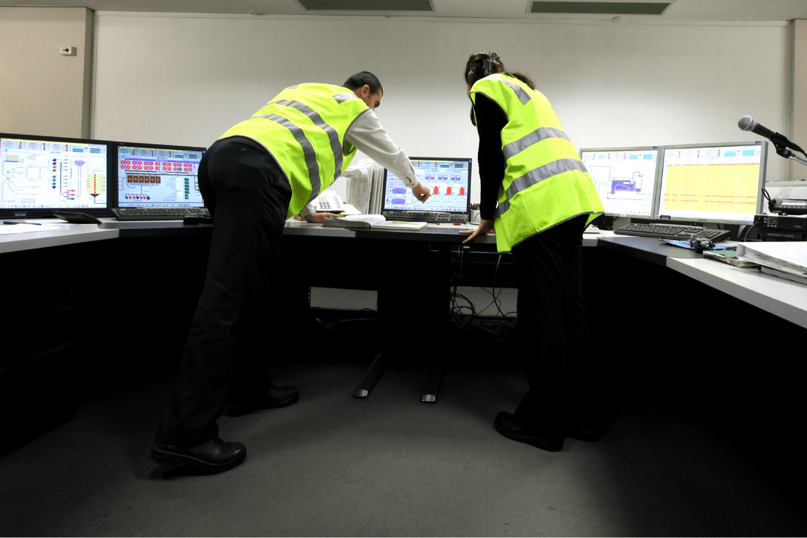 Man and woman in high Viz vests pointing at computer screens